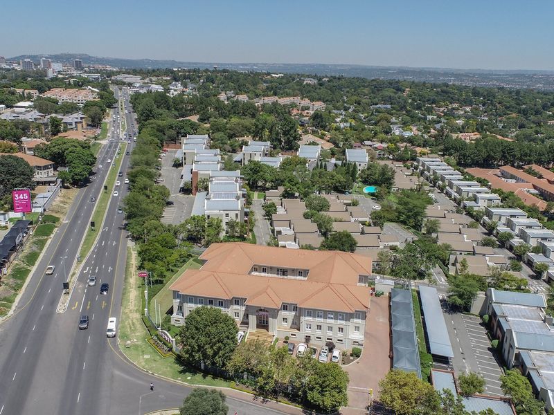 Aerial view of a commercial office complex featuring a main building with a tiled roof, extensive parking facilities, and landscaped grounds.