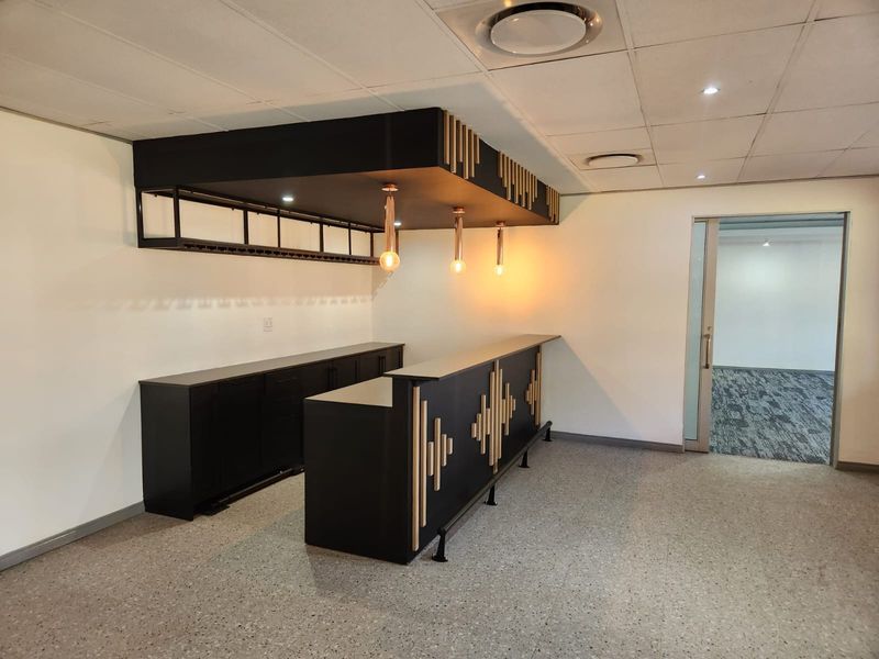 A modern, well-maintained commercial bar area featuring a sleek black built-in counter, suspended canopy with pendant lighting, and durable terrazzo flooring.