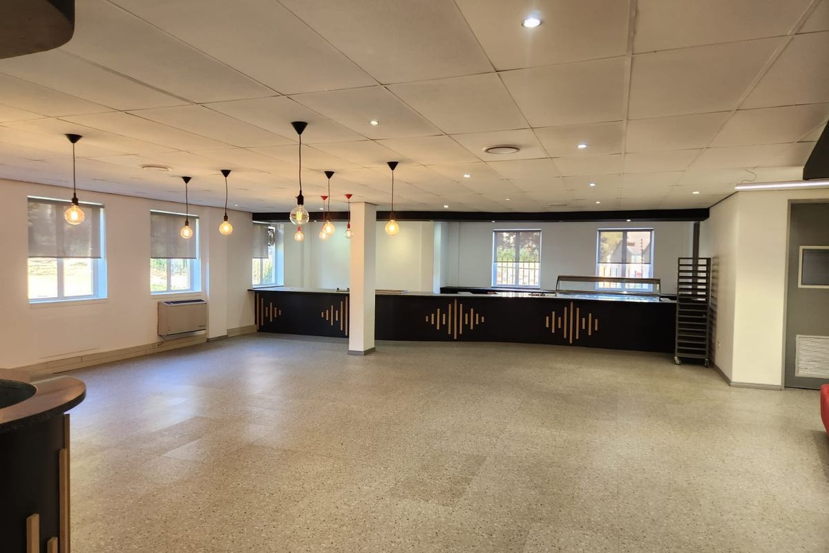 Spacious open-plan commercial area featuring terrazzo flooring, a built-in service counter, suspended ceiling with integrated lighting, and large windows for natural light.