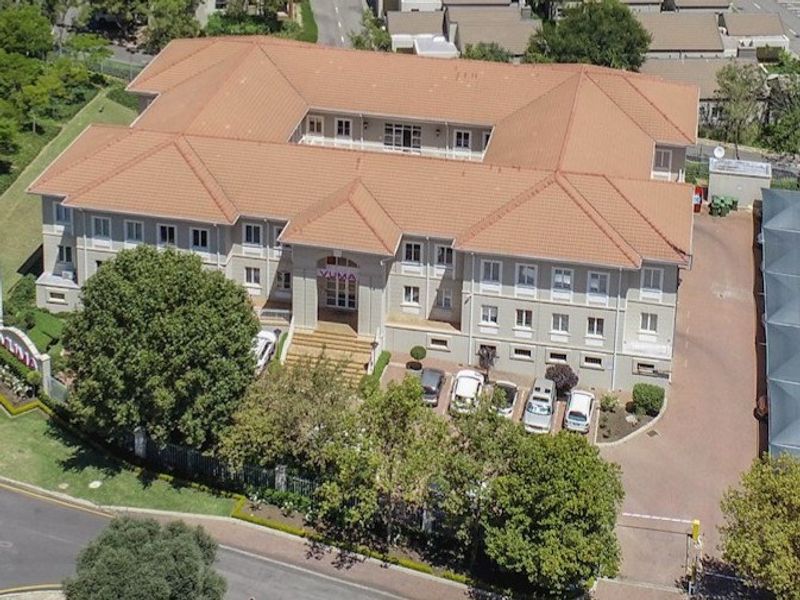 Aerial view of a multi-story commercial office building featuring a central courtyard, tiled roof, and paved parking area with secure access.