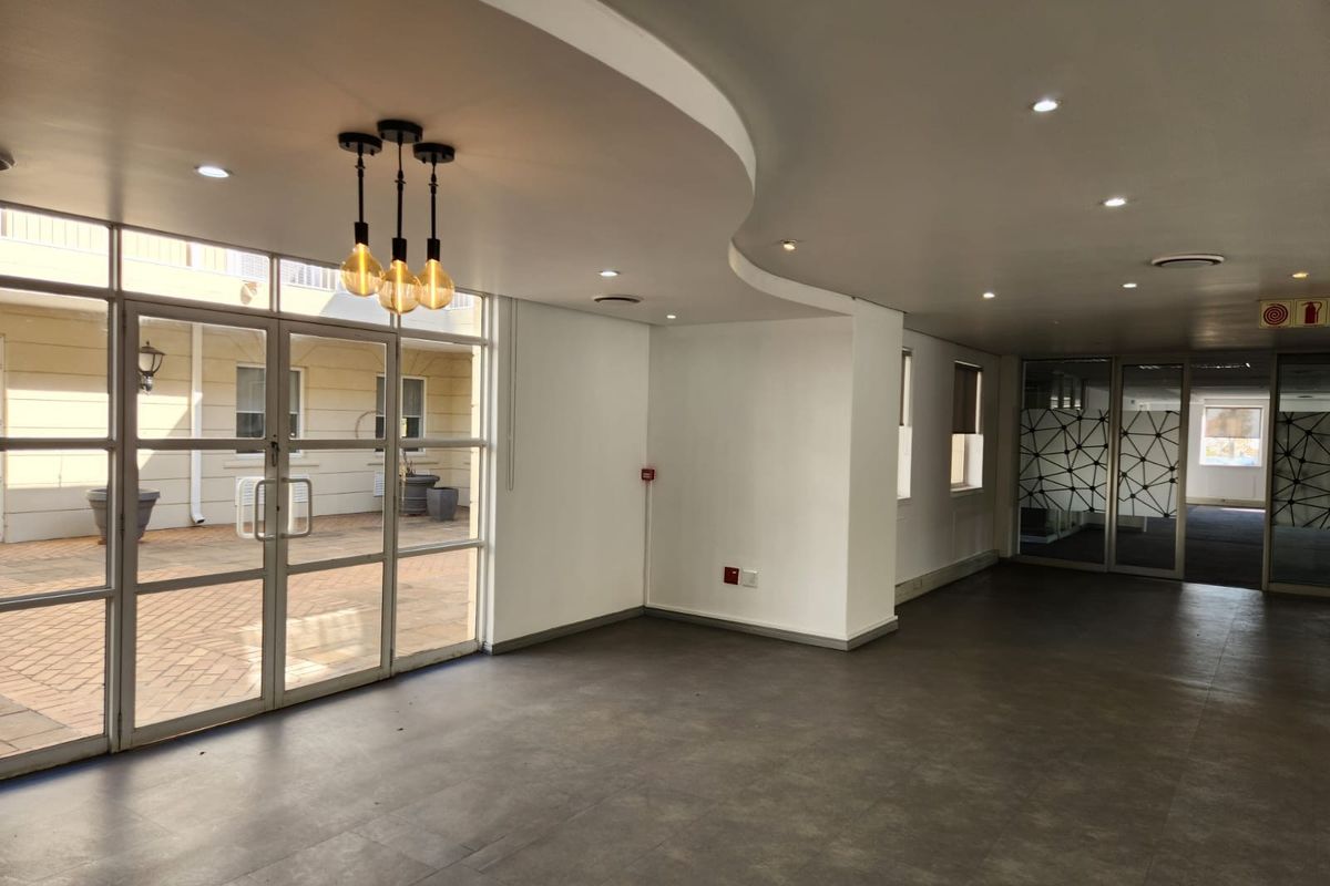 Spacious open-plan commercial area featuring modern recessed lighting, tiled floors, and large glass doors providing access to an outdoor courtyard.