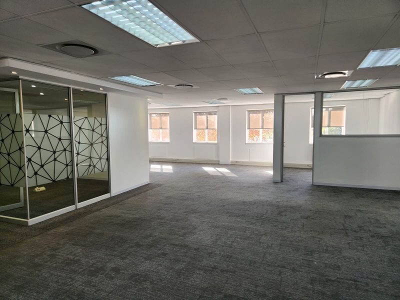 Spacious open-plan office area featuring glass-partitioned meeting rooms, suspended ceilings with recessed lighting, and neutral carpeting throughout.