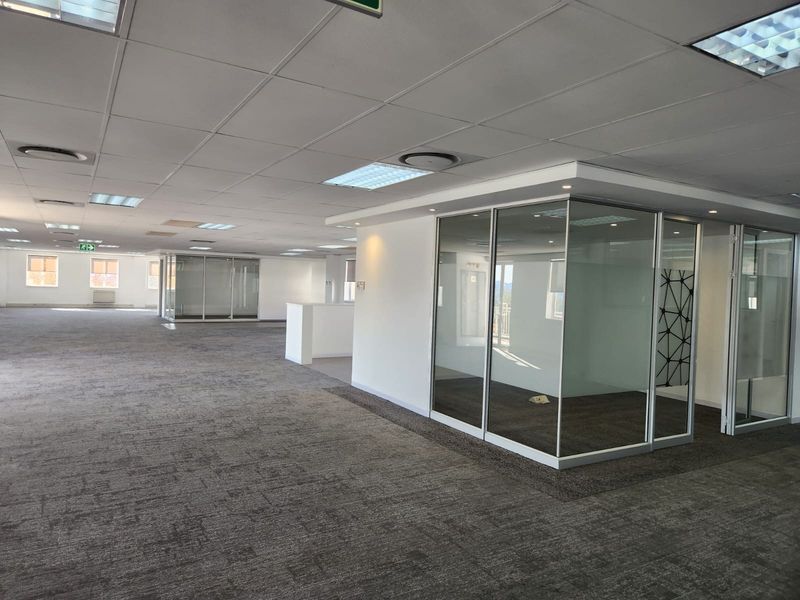 Spacious open-plan commercial office area featuring modern glass-partitioned meeting rooms, suspended ceilings, and neutral carpeted flooring throughout.