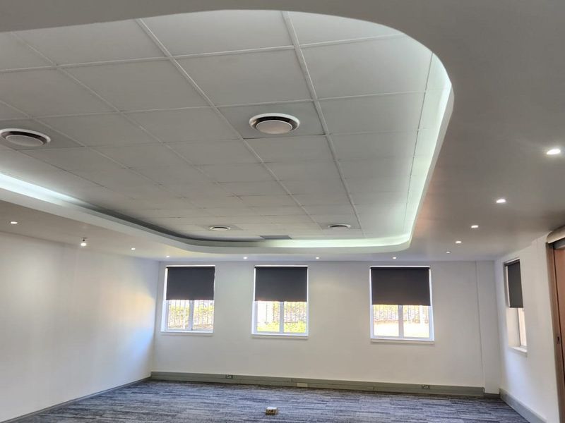 A bright, open-plan office space featuring a modern suspended ceiling with integrated cove lighting, recessed spotlights, and neutral carpet flooring.