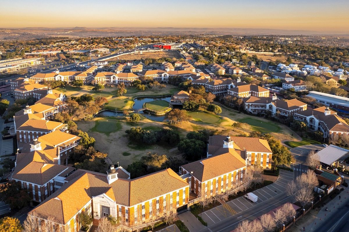 Aerial view of a large commercial office park complex featuring multiple brick buildings, tiled roofs, central landscaped gardens, and extensive parking facilities.