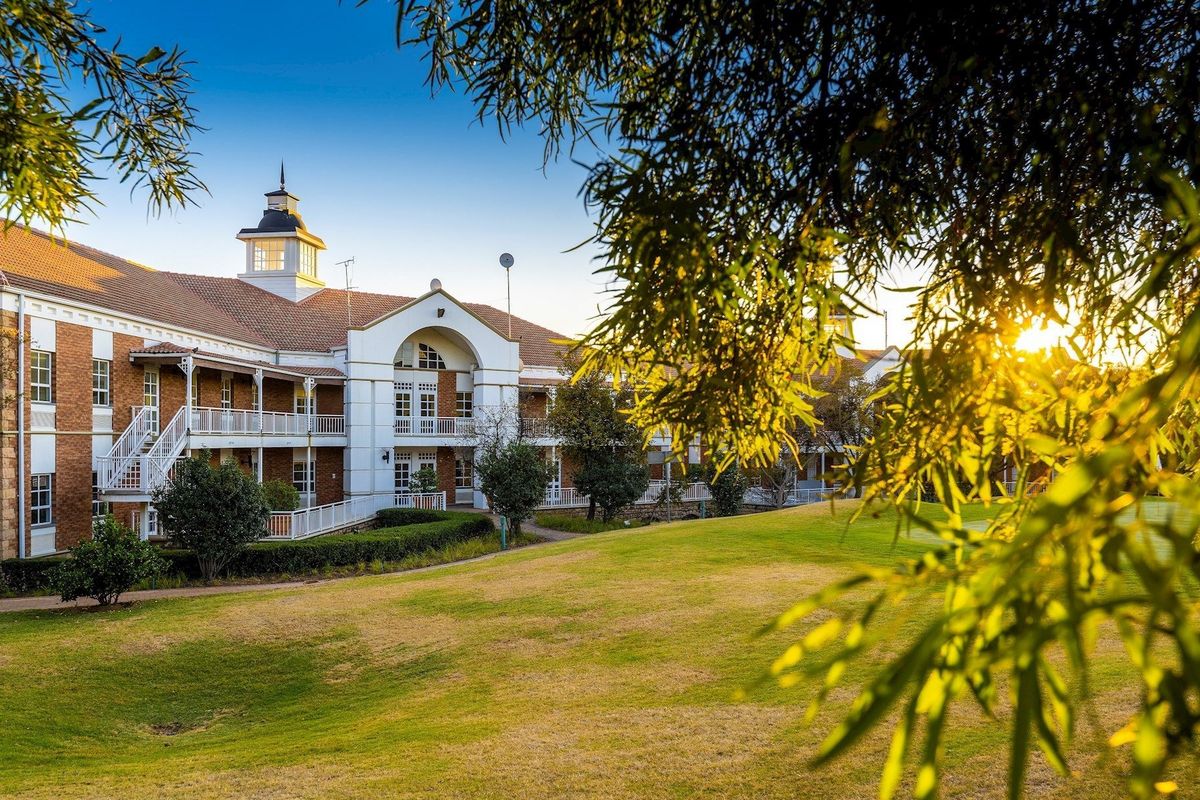 A well-maintained commercial building featuring a classic brick facade, multiple balconies, and a distinctive cupola, set against a beautifully landscaped lawn.