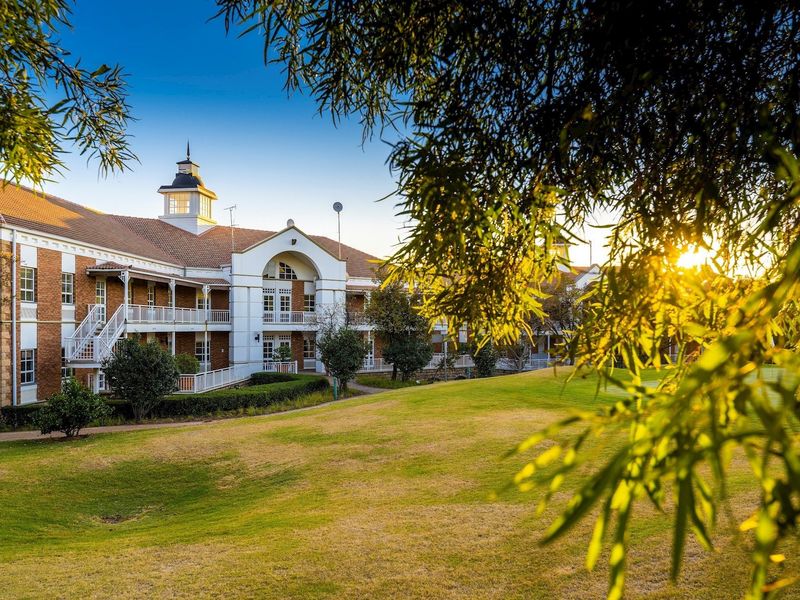 A well-maintained commercial building featuring a classic brick facade, multiple balconies, and a distinctive cupola, set against a beautifully landscaped lawn.