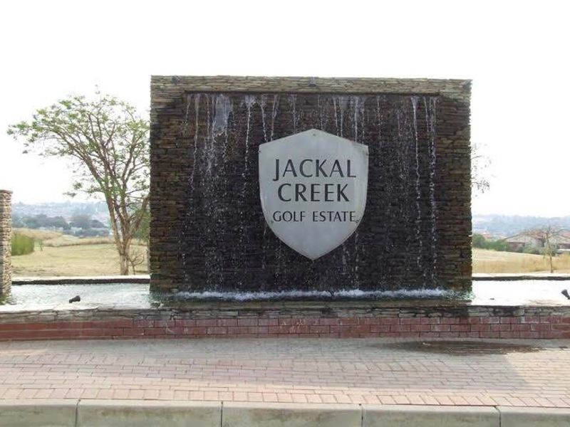 The entrance to Jackal Creek Golf Estate featuring a prominent stone water feature and paved driveway area.