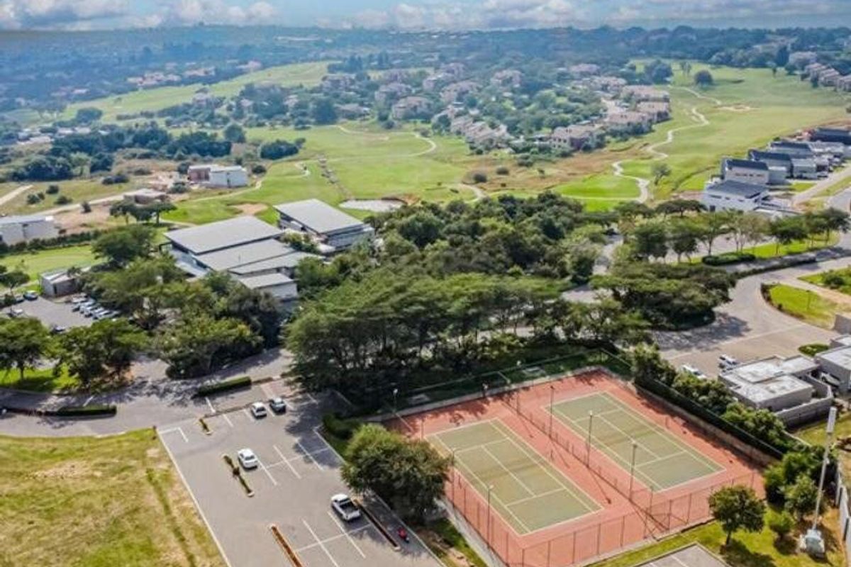 Aerial view of the estate featuring tennis courts, paved parking facilities, and surrounding landscaped green spaces within a residential community.