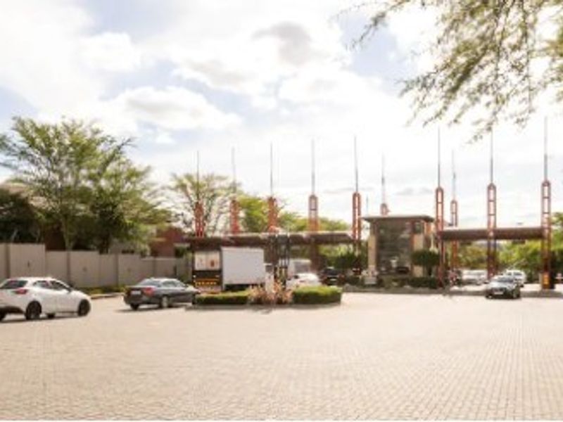 The main entrance and security gatehouse of the townhouse complex, featuring paved access and established perimeter landscaping.