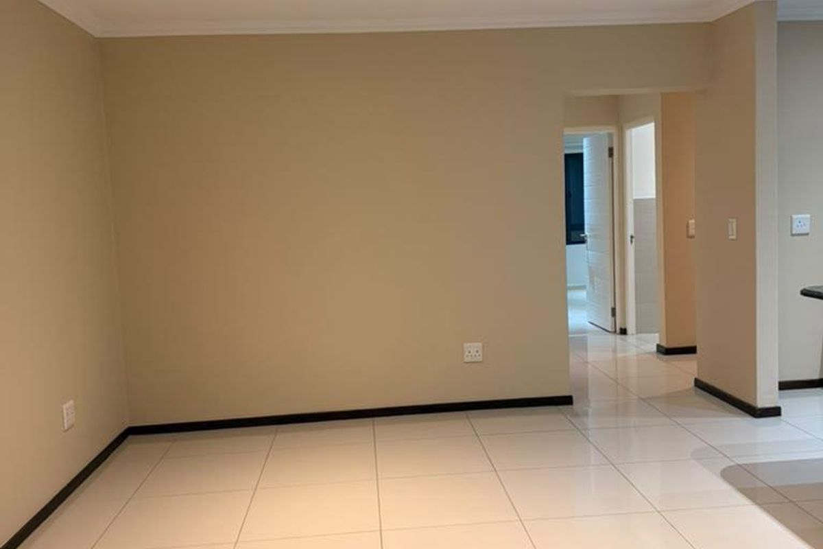 A bright, empty living area featuring neutral walls, modern porcelain floor tiles, and recessed downlighting, offering a clean and versatile space.