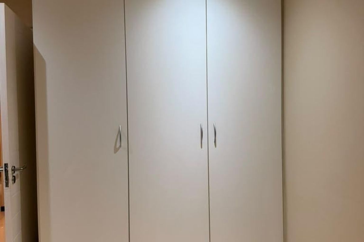 A clean, modern bedroom featuring neutral walls, light wood-look laminate flooring, and a large, floor-to-ceiling built-in wardrobe with recessed lighting.