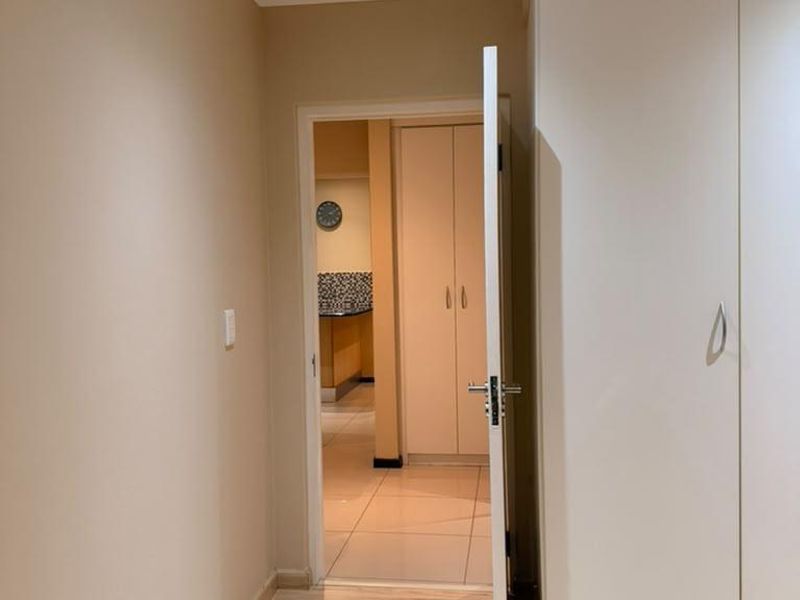 A clean, neutral hallway featuring light laminate flooring, built-in cupboards, and recessed downlighting, providing a seamless transition between living spaces.