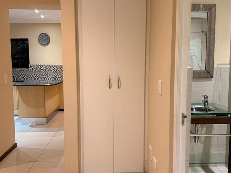 A clean hallway featuring neutral tiled flooring, a built-in storage cupboard, and access to the adjacent kitchen and bathroom areas.