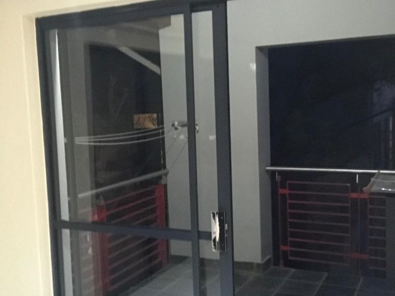 A covered balcony area featuring dark tiled flooring, a sliding glass door, and a metal safety railing.