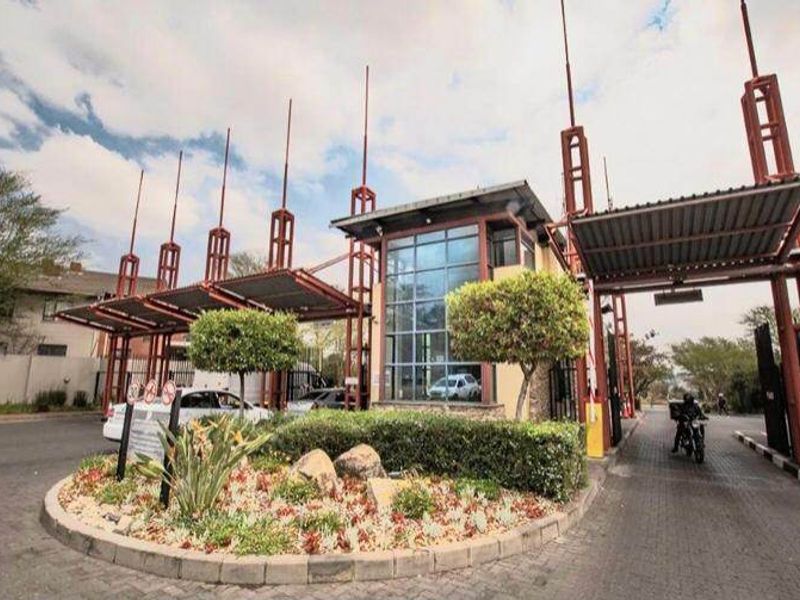 The main entrance to the townhouse complex featuring a modern security gatehouse, boom gates, and a landscaped traffic island.