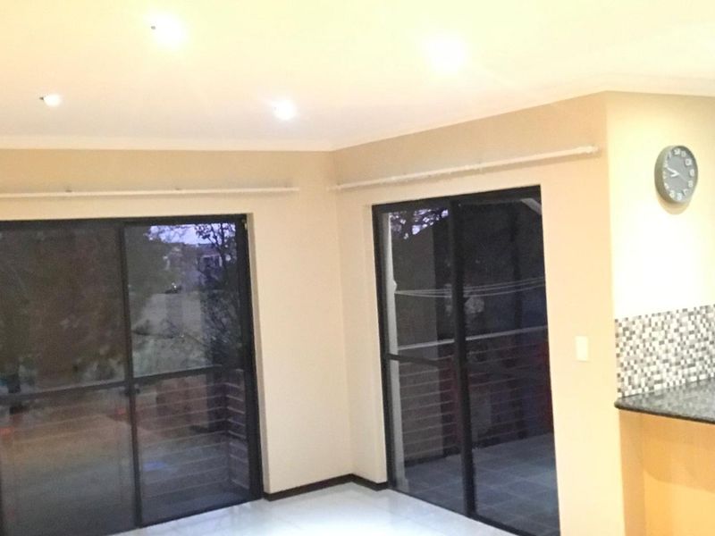 Open plan living area featuring tiled flooring, recessed lighting, and dual sliding glass doors leading to an outdoor space, with a partial kitchen counter visible.