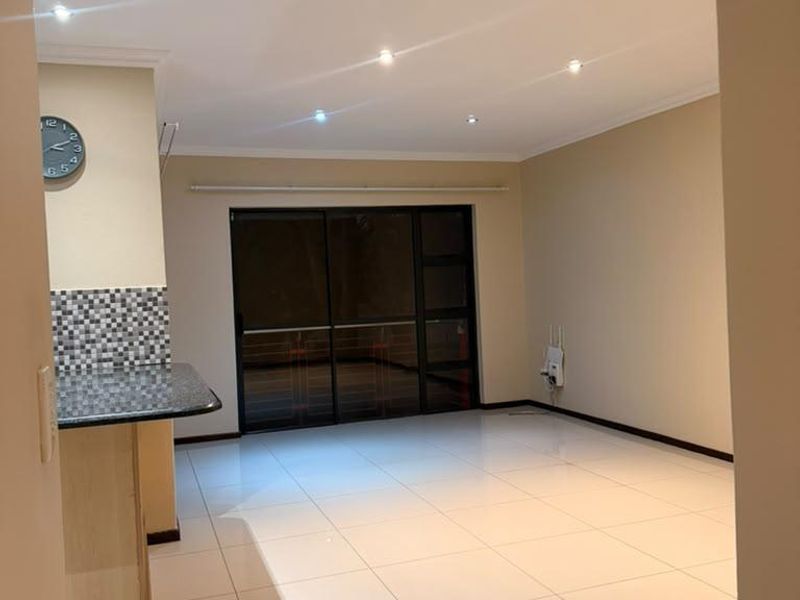 Spacious open-plan living area featuring neutral tiled flooring, recessed lighting, and a breakfast counter, leading to a sliding glass door.