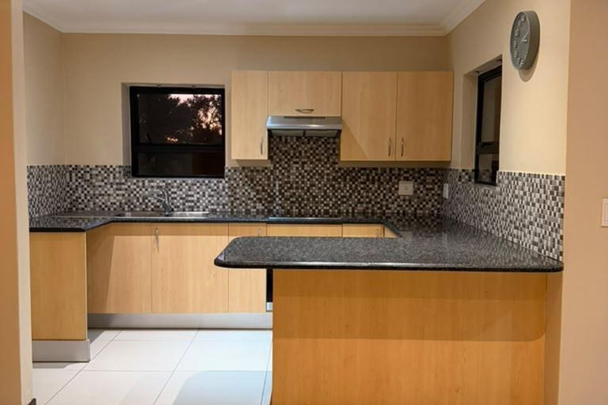 A clean, functional kitchen featuring light wood cabinetry, dark granite countertops, a mosaic tile backsplash, and a breakfast bar with recessed lighting.