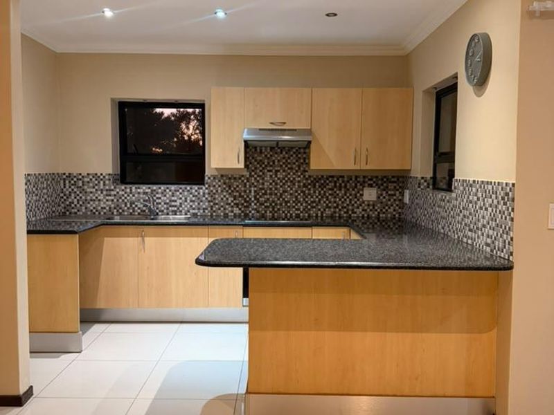 A clean, functional kitchen featuring light wood cabinetry, dark granite countertops, a mosaic tile backsplash, and a breakfast bar with recessed lighting.