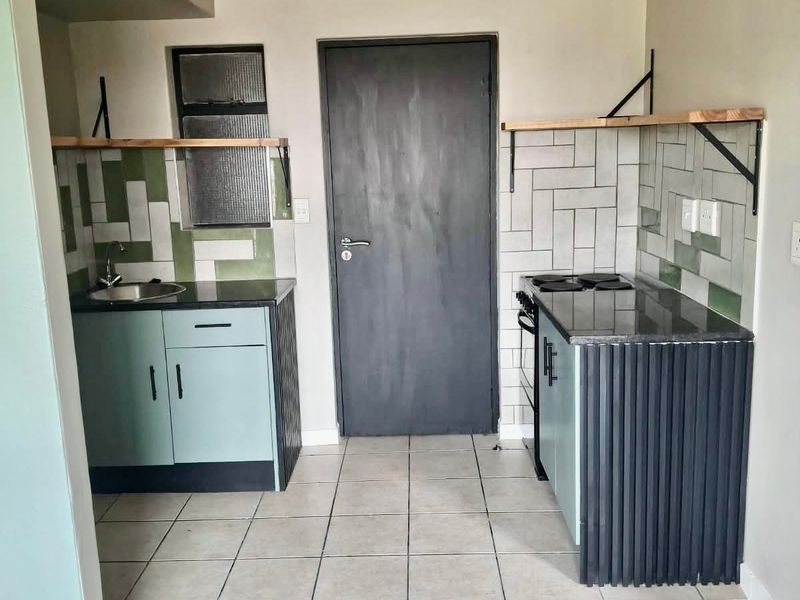A compact, functional kitchen featuring built-in cabinetry, stone countertops, a tiled backsplash, and an electric stove, presented in a clean, empty space.