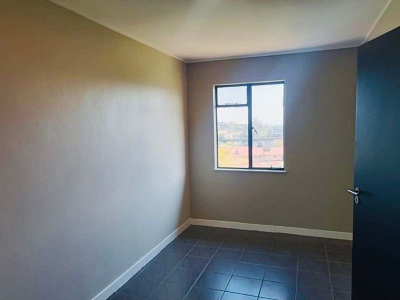 A clean, empty bedroom featuring neutral wall tones, dark tiled flooring, and an aluminium-framed window providing natural light.