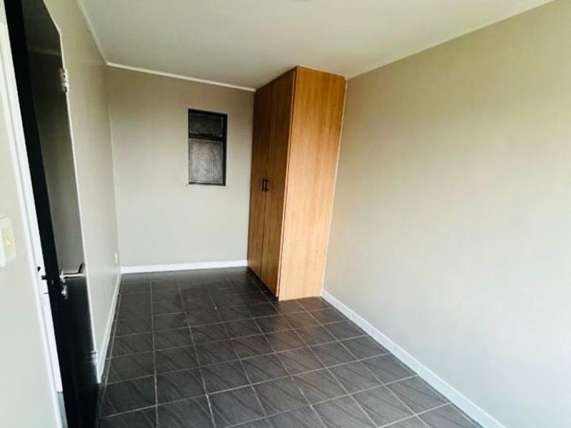 A compact, empty bedroom featuring dark tiled flooring, neutral walls, and a built-in wooden wardrobe.