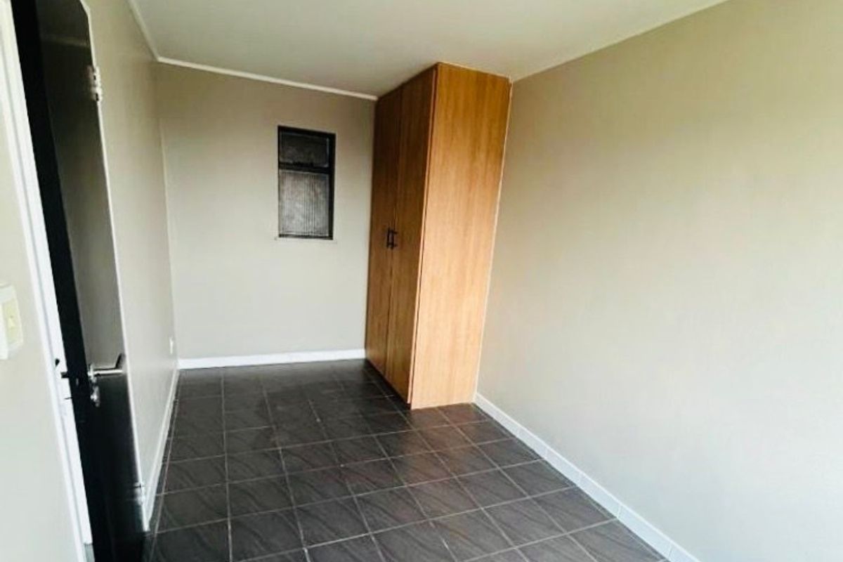A compact, empty bedroom featuring dark tiled flooring, neutral walls, and a built-in wooden wardrobe.