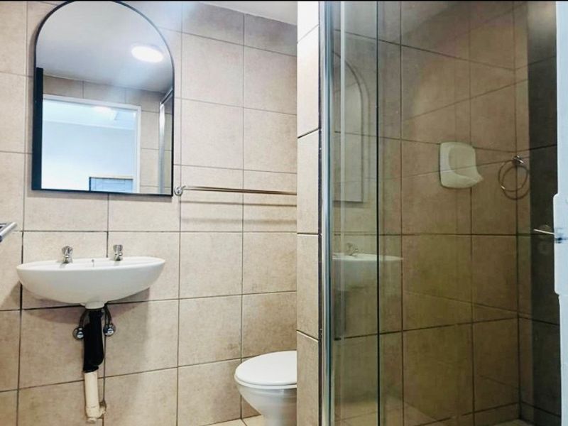 A functional bathroom featuring a wall-mounted basin, a glass-enclosed shower, and neutral wall tiling.