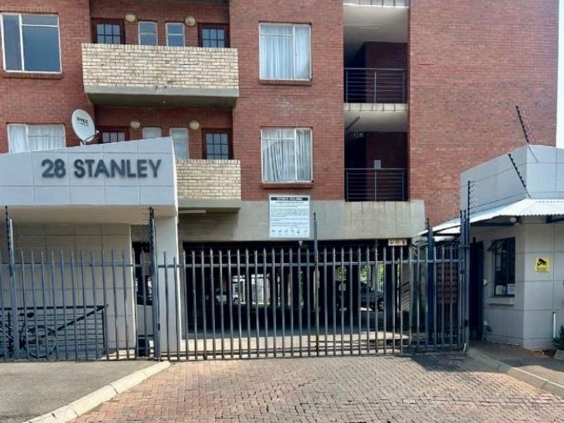 Front elevation of a brick apartment complex featuring a secure gated entrance, electric fencing, and a dedicated guard house.