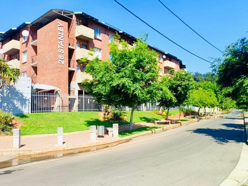 Street view of the brick apartment building facade featuring balconies, secure perimeter fencing, and a well-maintained landscaped walkway.