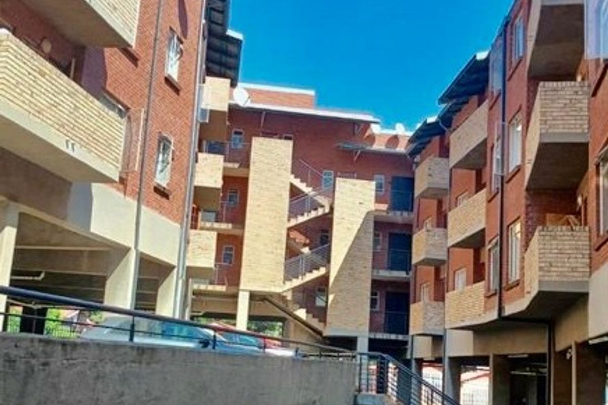 Exterior view of a multi-story apartment complex featuring exposed brick facades, concrete staircases, and private balconies.