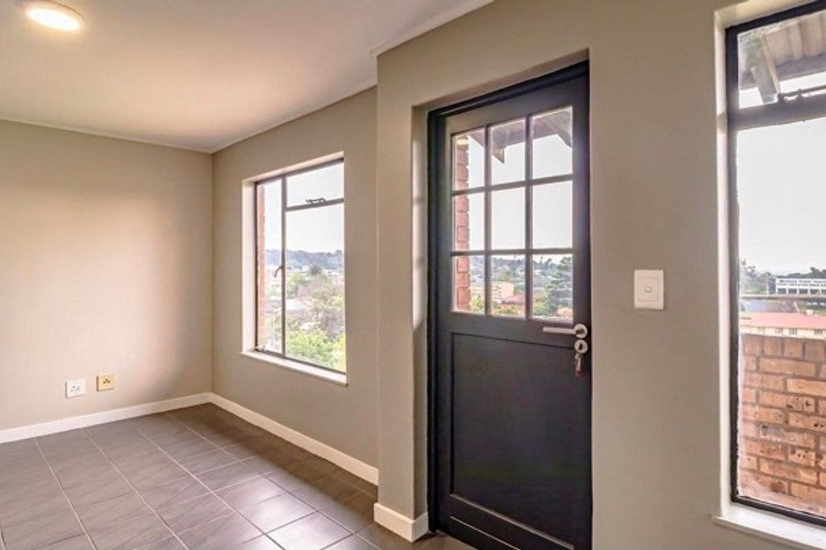 A bright, empty living area featuring neutral walls, tiled flooring, and large windows providing natural light and exterior views.