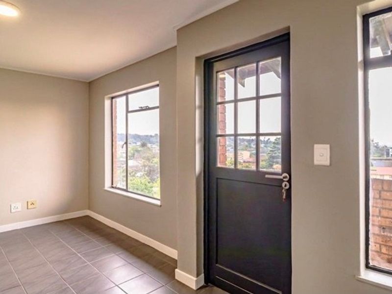A bright, empty living area featuring neutral walls, tiled flooring, and large windows providing natural light and exterior views.