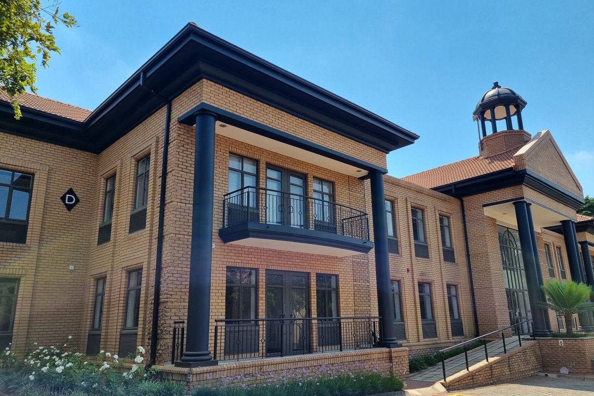 A well-maintained commercial building featuring a classic brick facade, decorative columns, a balcony with iron railings, and a distinctive roof cupola.