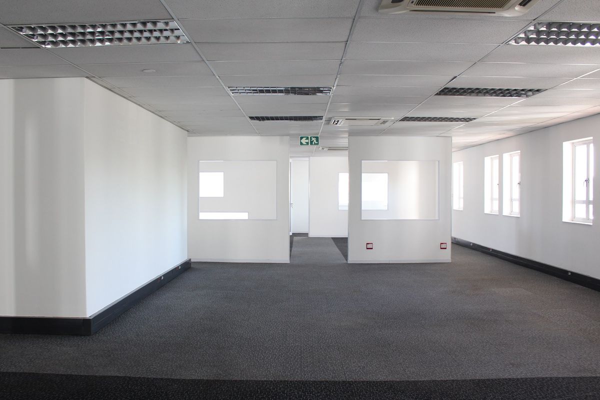 A spacious, vacant commercial office area featuring neutral finishes, suspended ceilings with recessed lighting, ducted air conditioning, and internal glass partitions.