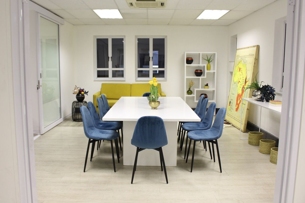 A well-lit commercial office space featuring a central meeting table, suspended ceiling with recessed lighting, and modern laminate flooring.