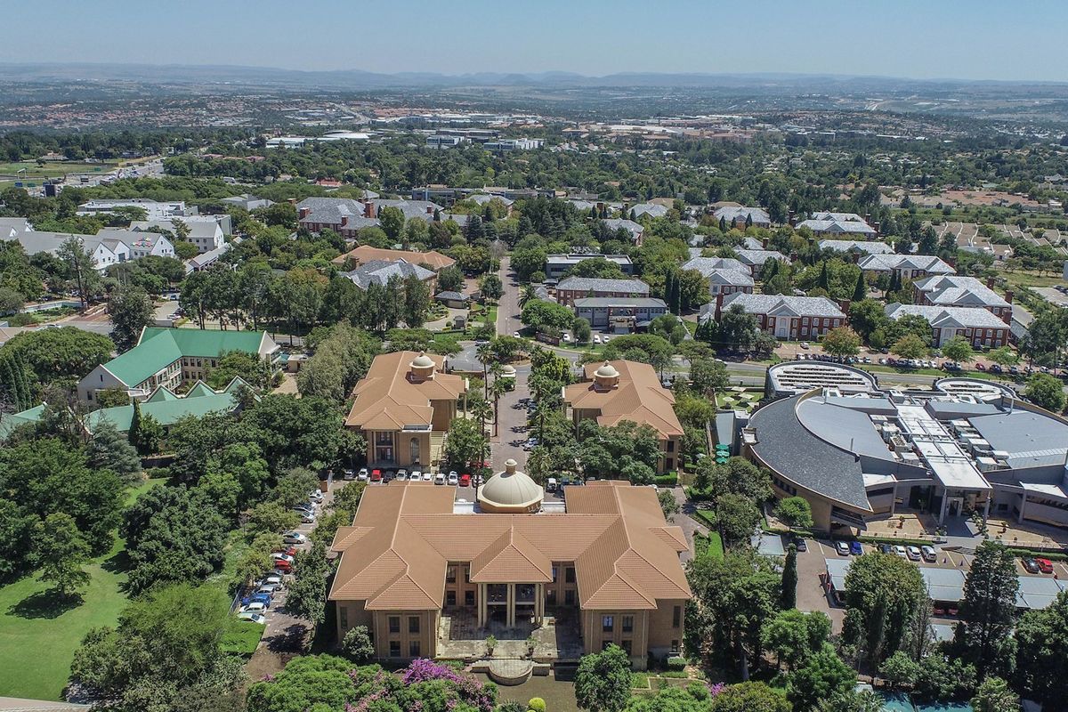 An aerial view of a commercial office park featuring multiple buildings with tiled roofs, surrounded by mature trees and landscaped grounds.