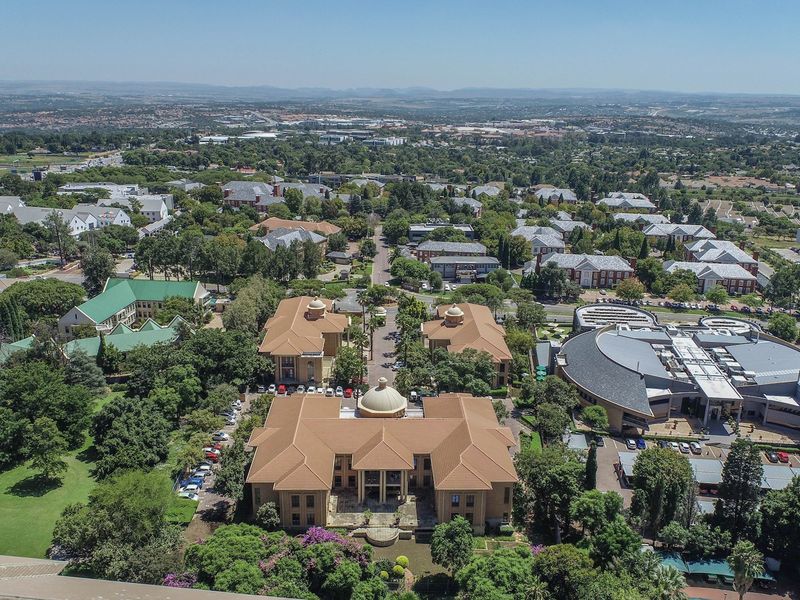 An aerial view of a commercial office park featuring multiple buildings with tiled roofs, surrounded by mature trees and landscaped grounds.