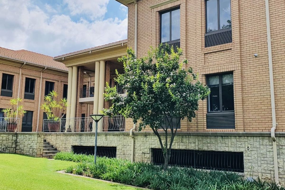A well-maintained commercial building exterior featuring brick and stone facade, classic columns, and a landscaped garden area with a balcony.