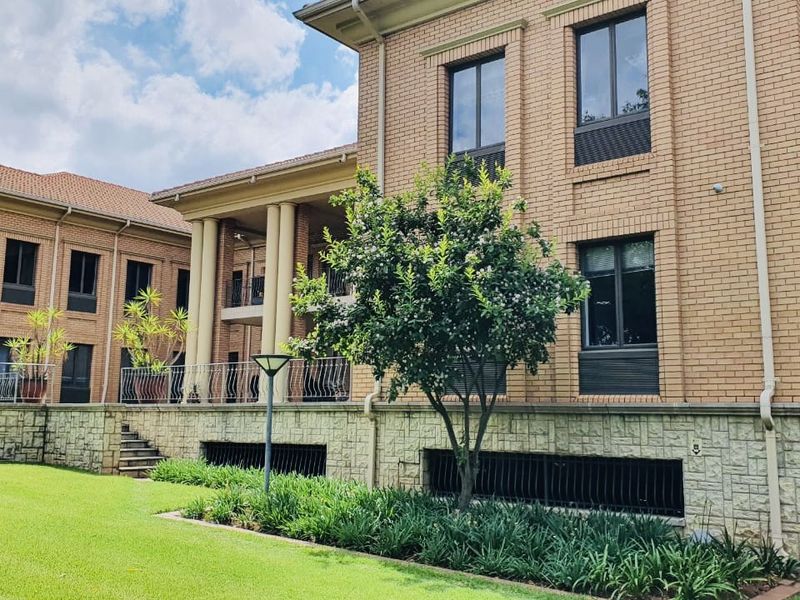 A well-maintained commercial building exterior featuring brick and stone facade, classic columns, and a landscaped garden area with a balcony.
