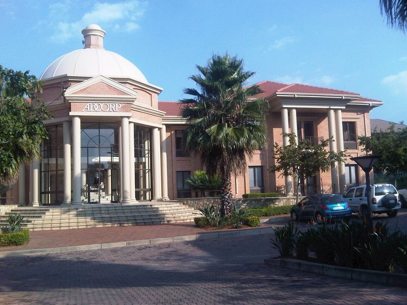 A professional commercial office building featuring a prominent domed entrance, classical columns, brick facade, and a paved driveway approach.
