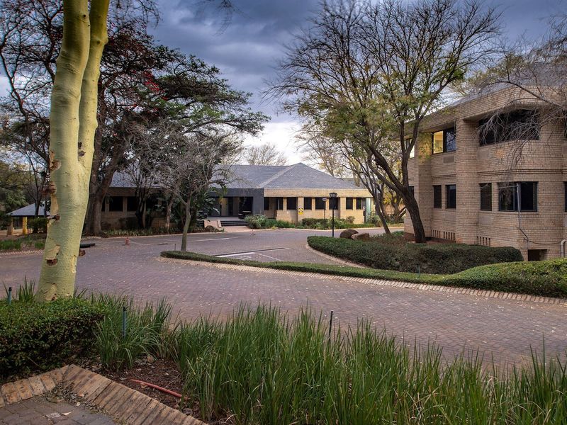 A view of the commercial property entrance featuring a brick paved driveway, mature landscaping, and face brick building facades.