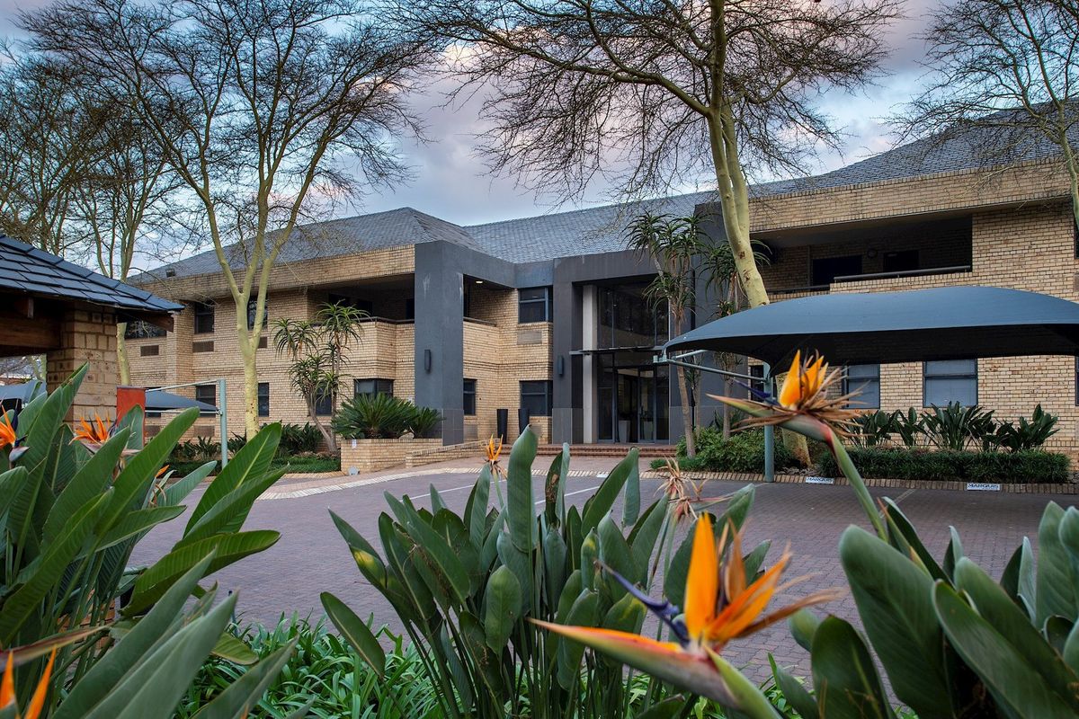 A professional exterior view of a multi-story commercial office building featuring brick masonry, a paved driveway, and covered parking bays.