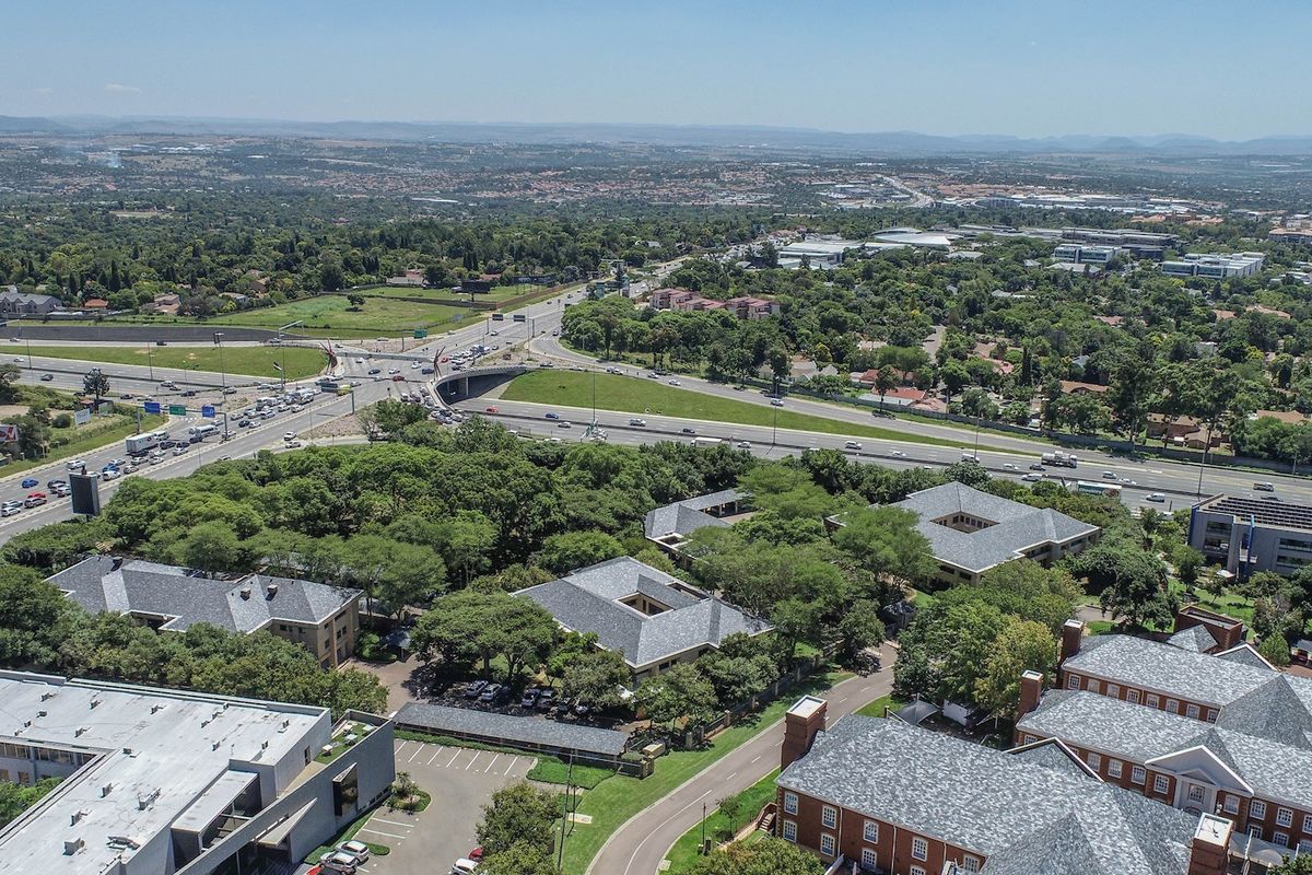 Aerial view of a commercial office park complex featuring multiple buildings with pitched roofs, surrounded by landscaped grounds and adjacent to a major highway.