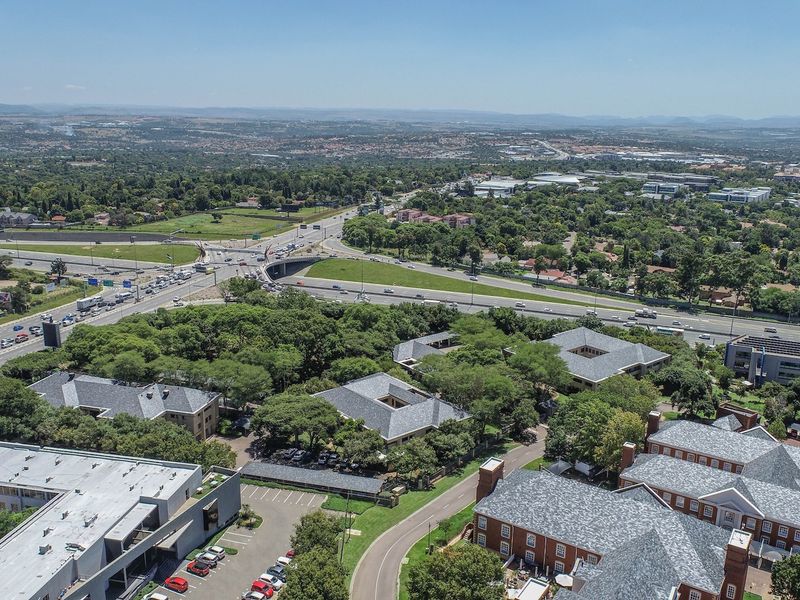 Aerial view of a commercial office park complex featuring multiple buildings with pitched roofs, surrounded by landscaped grounds and adjacent to a major highway.