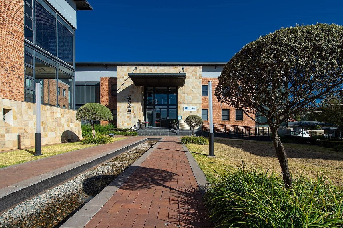 Professional exterior view of a modern commercial office building featuring brick and stone facade, glass entrance, and a landscaped paved walkway with water feature.