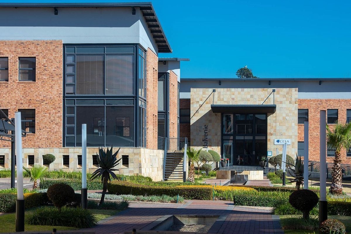 A professional view of the commercial building entrance featuring brick and stone facade, large glass windows, and a well-maintained landscaped garden.