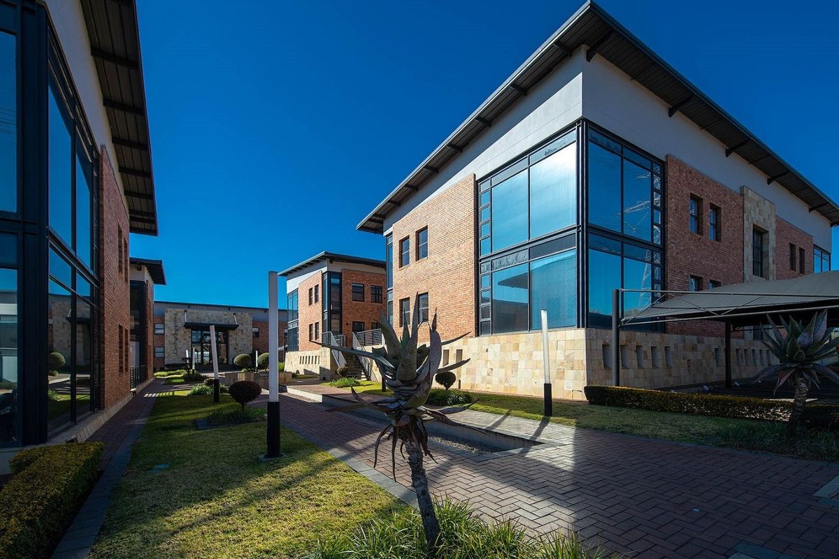 A modern commercial office complex featuring brick and stone facades, large glass windows, and well-maintained paved walkways and landscaped garden areas.