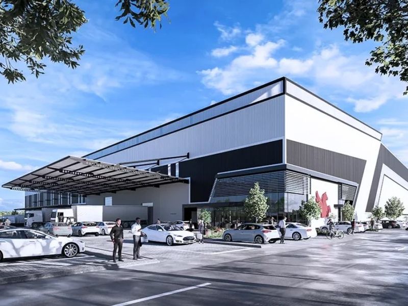 A modern industrial warehouse facility featuring a large loading canopy, extensive paved parking, and a contemporary glass and metal facade.